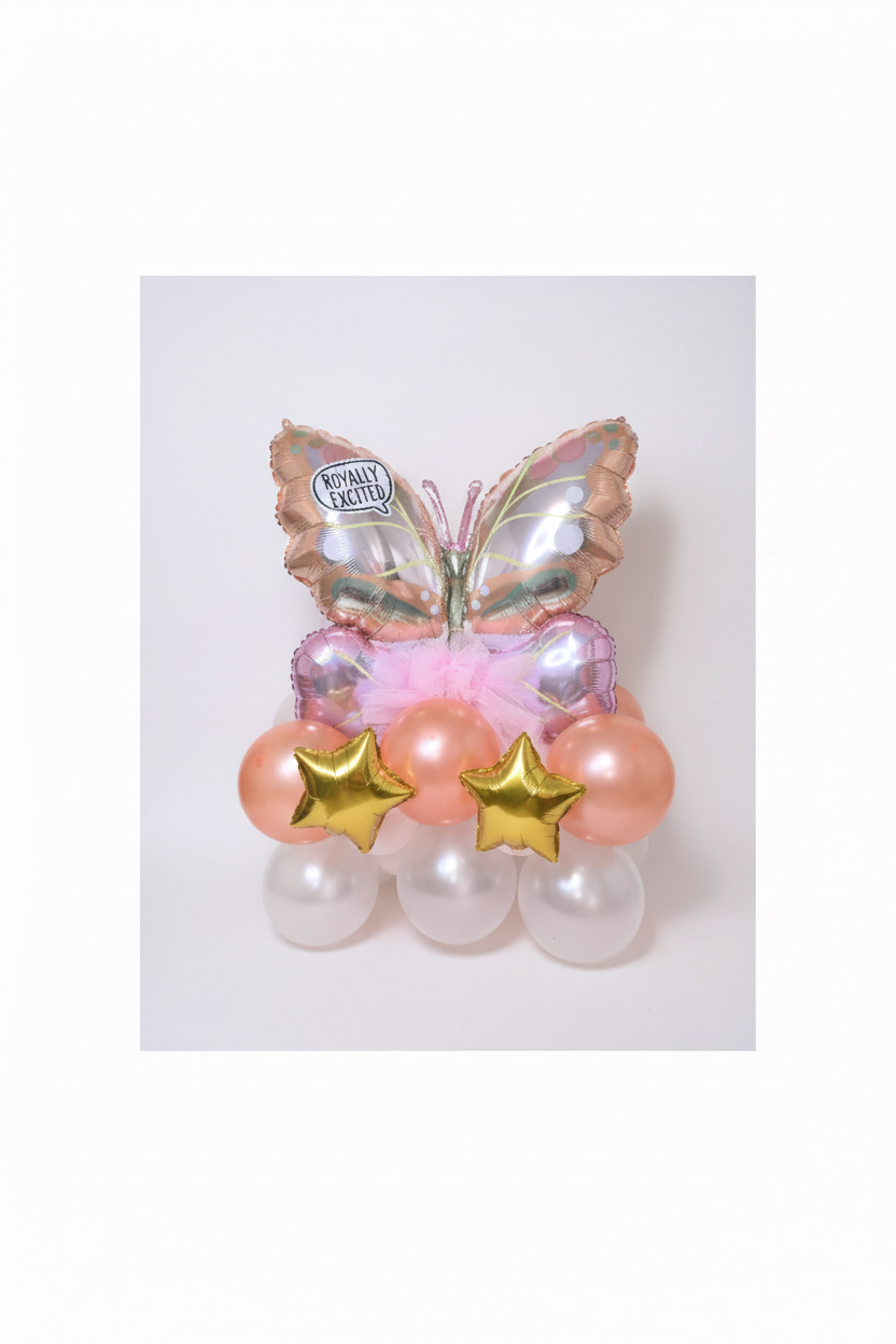A decorative balloon bouquet shaped like a butterfly, with iridescent pink and gold foil wings, peach balloons, pale pink balloons, and two metallic gold star balloons, set against a glittery gold backdrop.