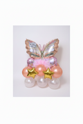 A decorative balloon bouquet shaped like a butterfly, with iridescent pink and gold foil wings, peach balloons, pale pink balloons, and two metallic gold star balloons, set against a glittery gold backdrop.